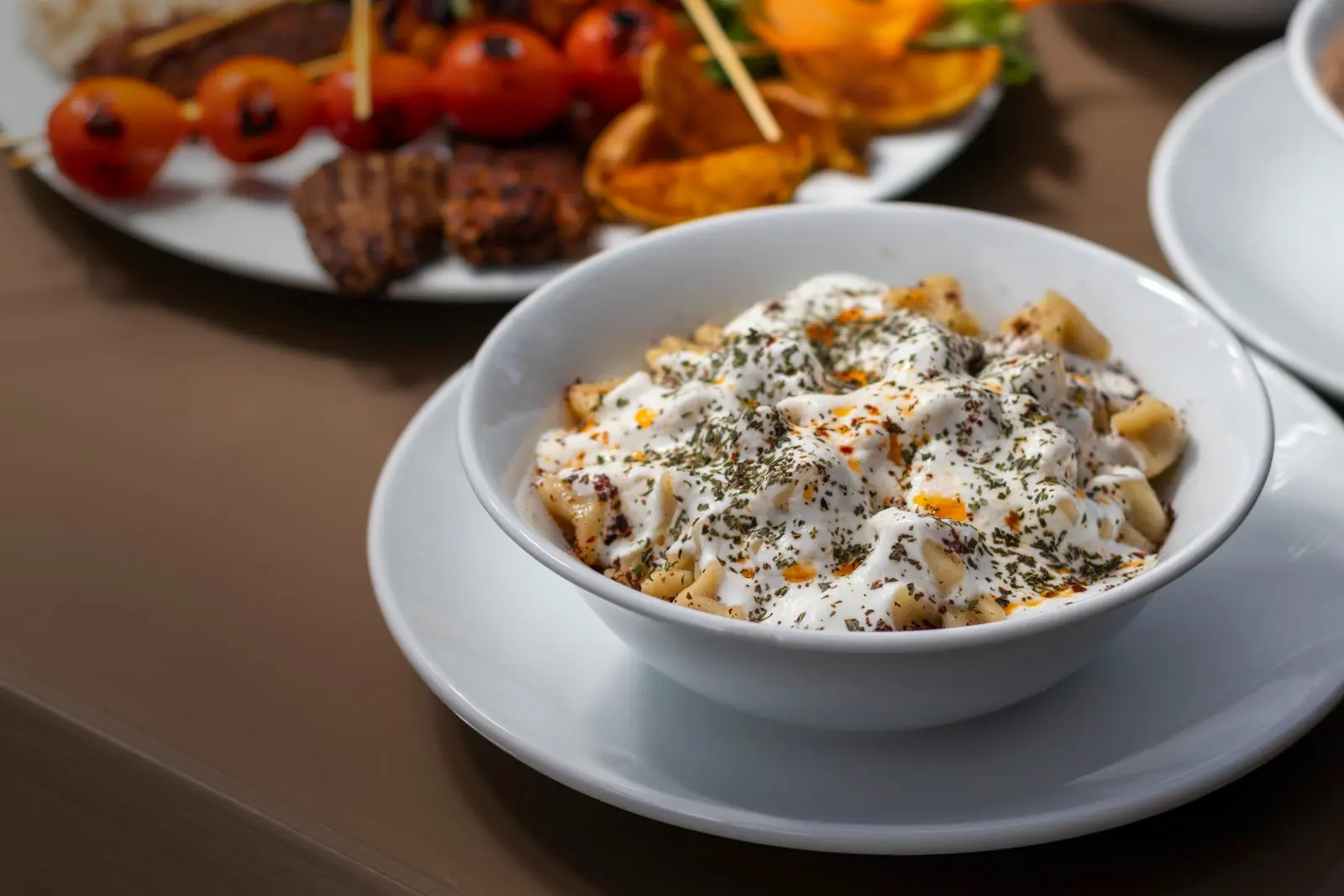 Mantı aan tafel, geserveerd met yoghurt, kruiden en een warme botersaus.